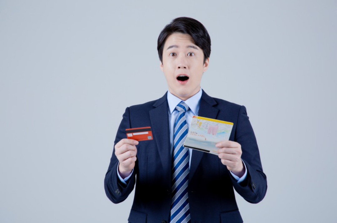 한 남성이 한손에는 카드를 한손에는 통장을 들고 놀라고 있다.