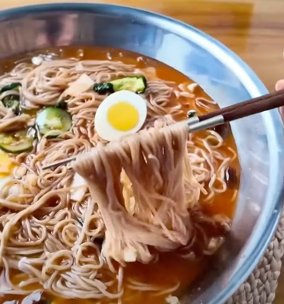스테인레스 용기안 계란이 얹어진 물냉면을 젓가락으로 든 모습