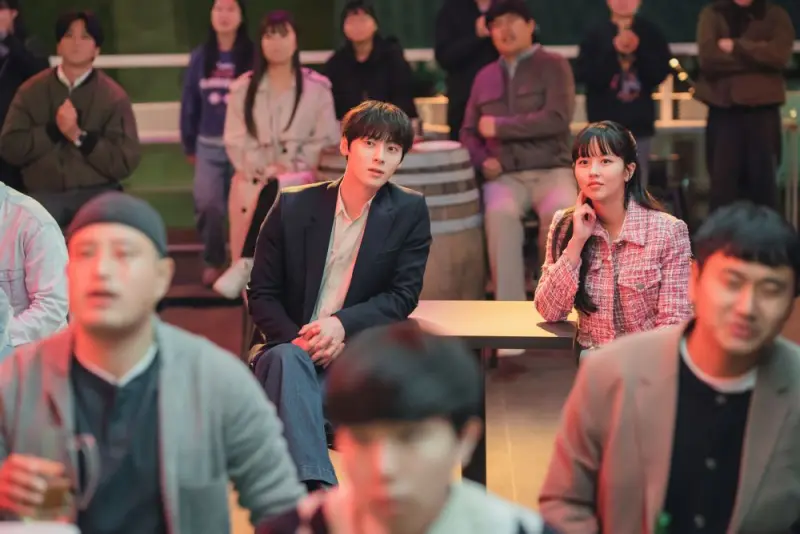 여러 사람들이 있는 가운데에 검은 자켓을 입고 앉아 있는 김도하와 옆에 나란히 앉아 있는 목솔희