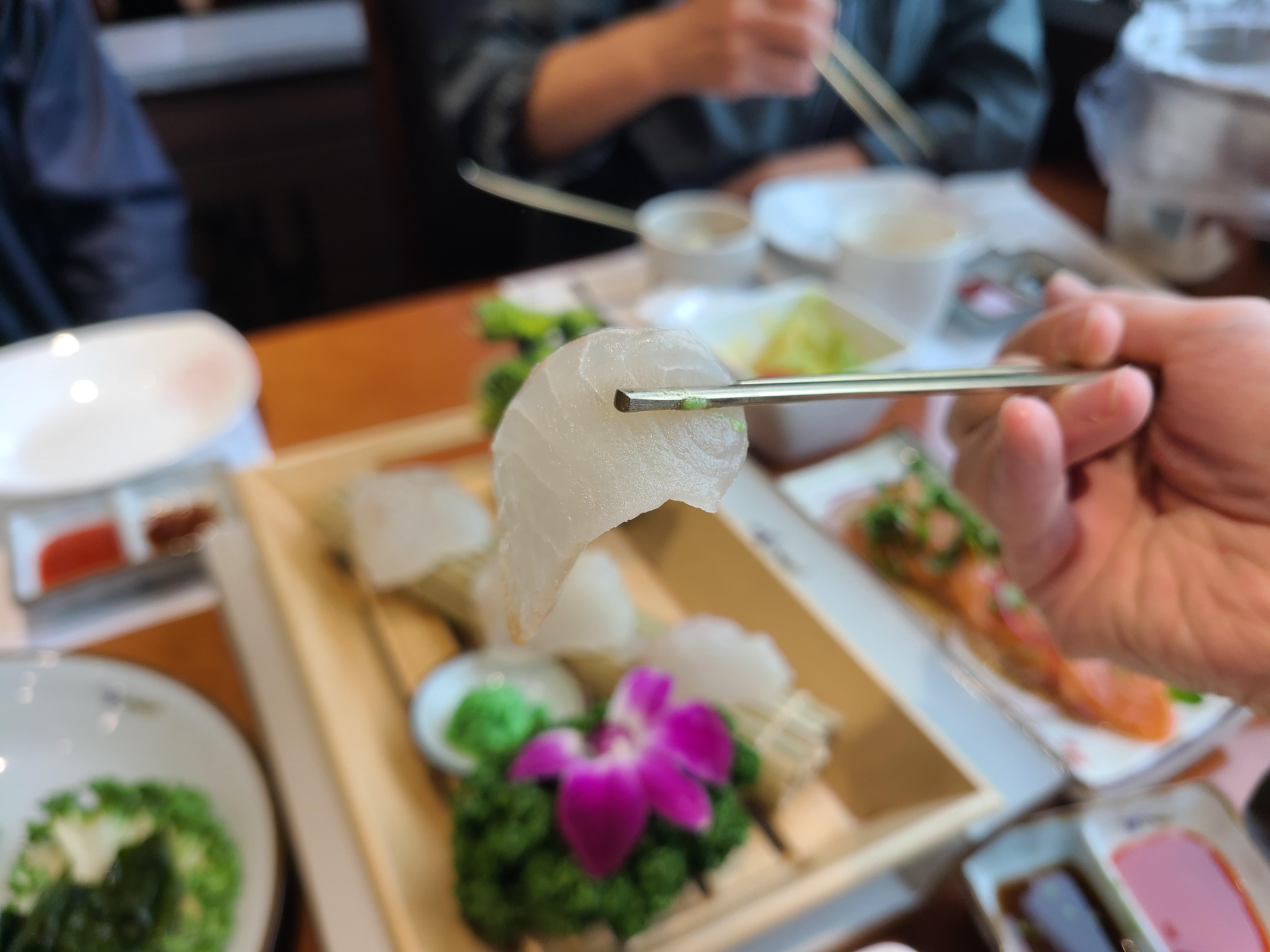 천안 대게나라 광어회 한점을 젓가락으로 든 모습