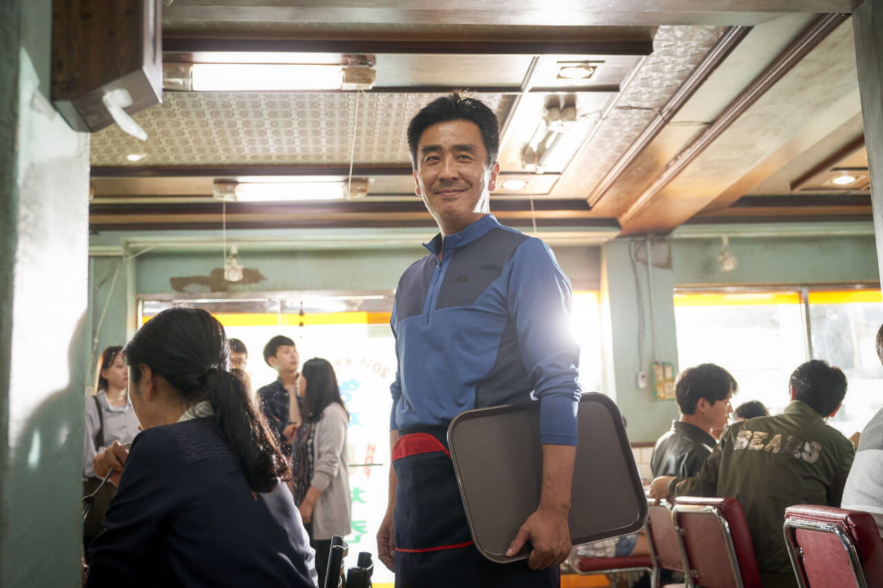 고상기 반장 역의 류승룡이 치킨집 사장님으로 일하며 웃고 있는 모습