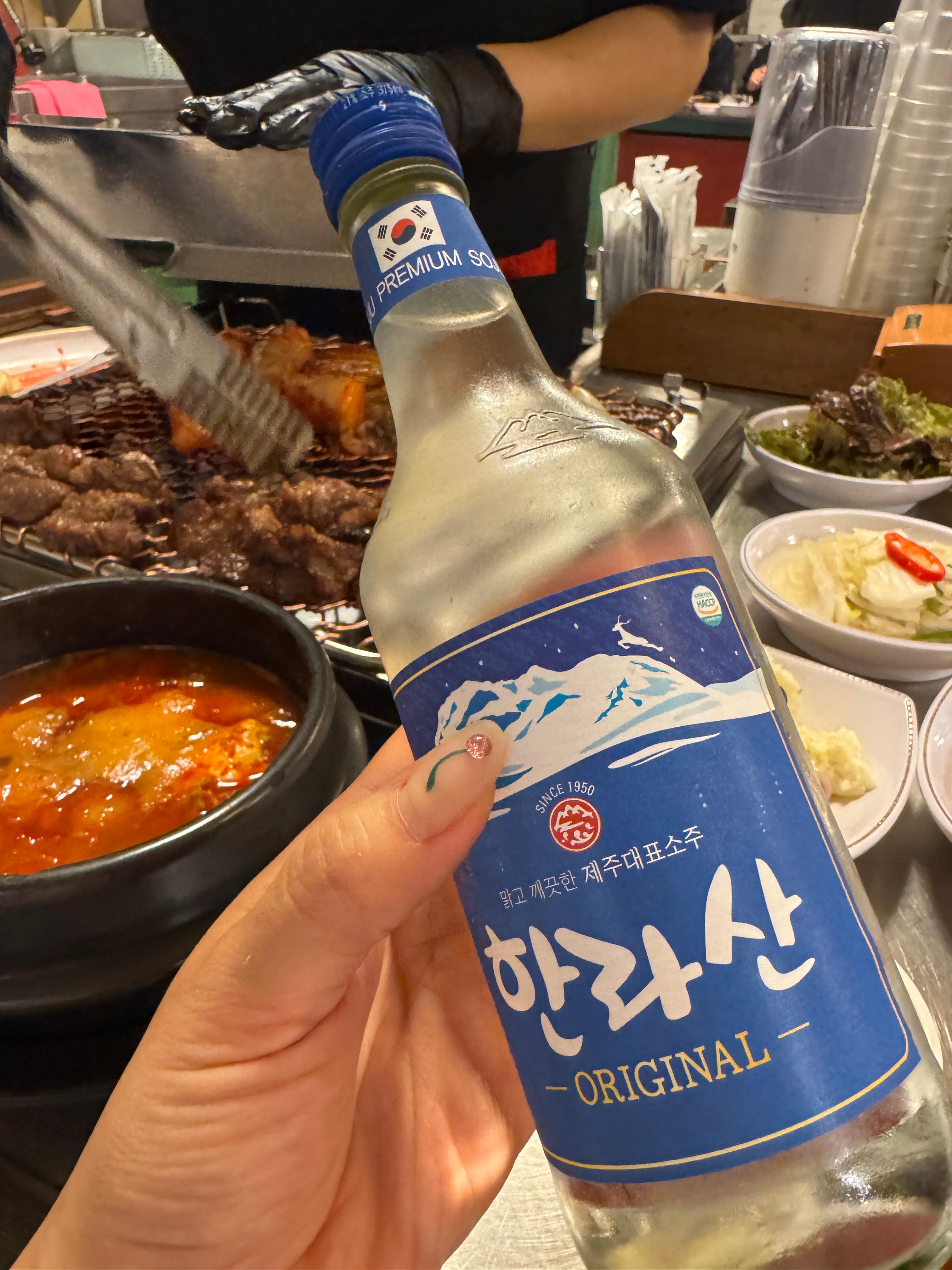 세광양대창 정자점 불판 앞에서 고기 굽는 장면과 함께 제주 한라산 소주병을 들고 있는 사진, 따뜻한 조명 아래에서 불판의 고소한 향과 소주의 시원함이 어우러진 모습