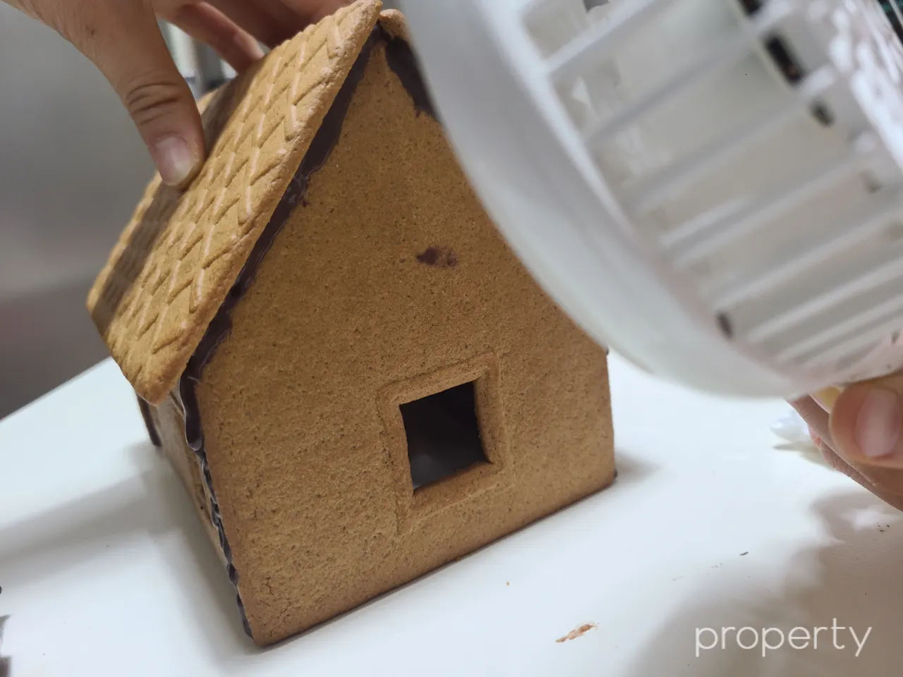 초콜릿으로이어붙인과자집-핸디선풍기로식히기-손으로과자집지붕을눌러주고있는