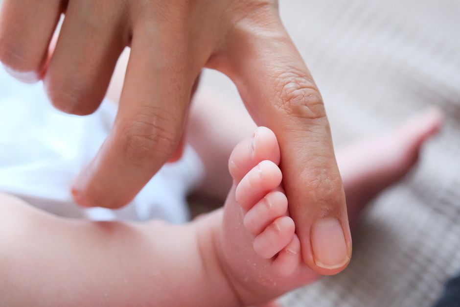 Close-up of an adult finger gently touching a baby's toes, emphasizing tenderness and care.