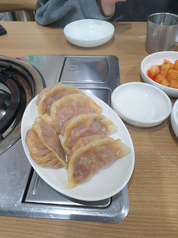 테이블 위에 김치 만두 5개가 올려져 있다. 옆에는 깍두기가 보인다.