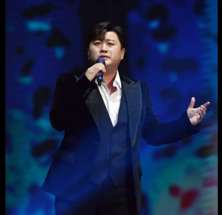 파란 무대배경 검은 옷을 입고 오른손으로 마이크를 든채 노래하는 김호중
