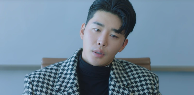 회의실을 배경으로 체크무늬 코트를 입고 상석에 앉아 있는 이 연애는 불가항력의 이현서 캐릭터