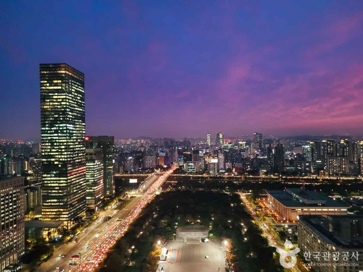 해 질 녘 보랏빛으로 물드는 서울 하늘, 빌딩 숲 사이로 켜지는 노란 조명