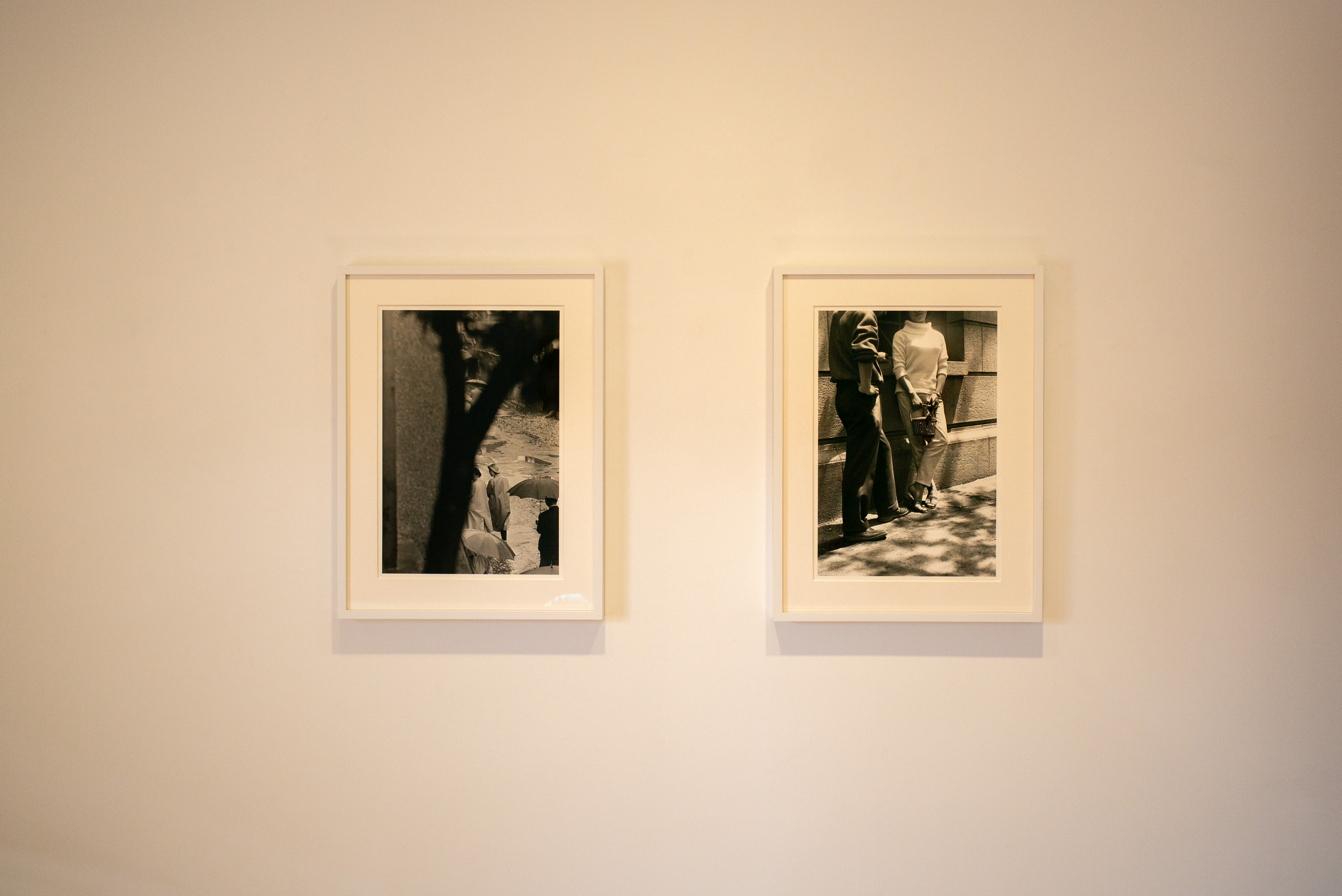 따뜻한 미색 벽면에 나란히 걸린 두 점의 흑백 인물 사진 액자와 실내 조명에 의한 부드러운 색감