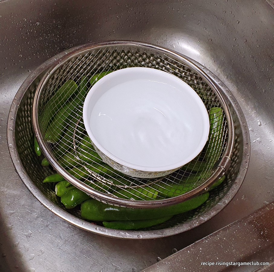 풋고추 된장무침에 들어갈 풋고추를 물 위에 떠오르지 않도록 무게가 있는 도구로 눌러 놓은 사진