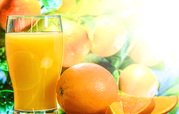 유리컵에 담긴 오렌지주스와 오른쪽에는 탱글탱글한 오렌지 한개랑 잘린 오렌지 조각들이 있다.