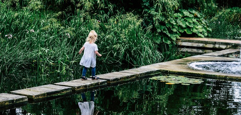 정원과 연못이 있고, 그 연못가를 걸어가는 어린 여자아이의 뒷모습이 보이는 사진