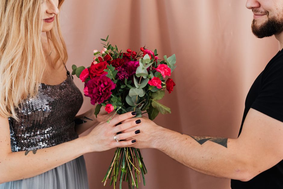 A man hands a vibrant flower bouquet to a woman in a sequined dress, creating a romantic mood.