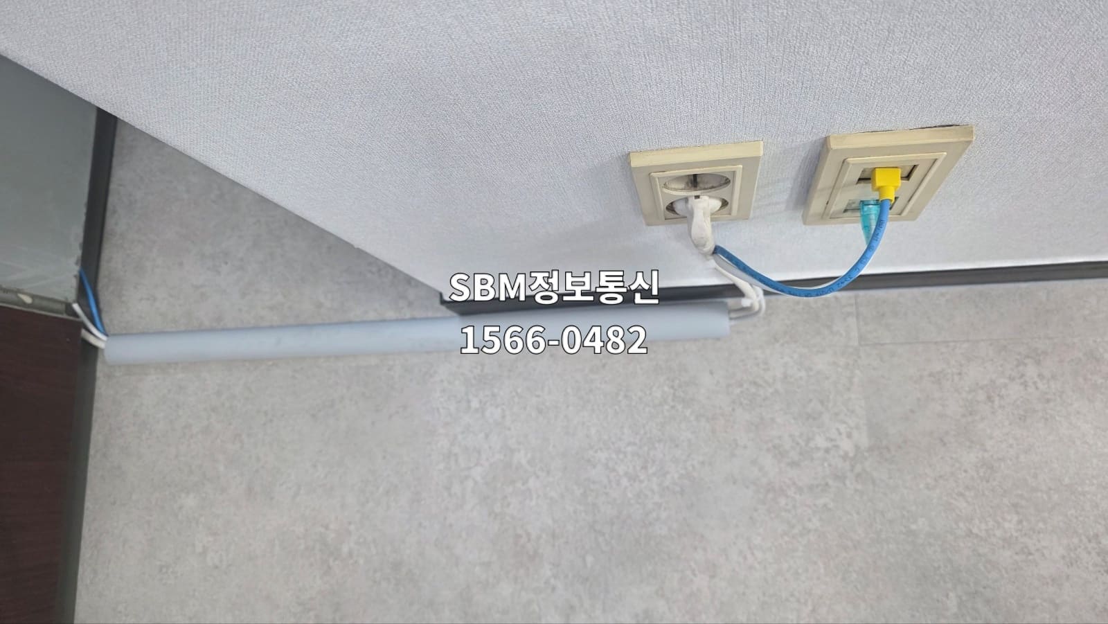 무실 벽면의 기존 통신 포트에서 파란색 랜선을 연결해 하단 회색 몰딩 내부로 선을 숨겨 포설하는 시작점
