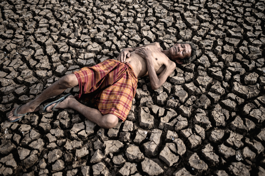 늙은 동양 남성이 무더위로 인해서 땅이 말라서 쩍쩍 갈라진 곳에 반바지만 입고 누워 있는 것을 찍은 사진
