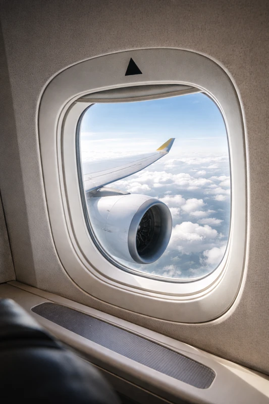 항공기 객실 창문 위에 있는 작은 검은색 삼각형 표시(▲)와 창밖으로 보이는 항공기 엔진과 날개, 구름 위 하늘 풍경을 함께 담은 항공기 객실 내부 모습.