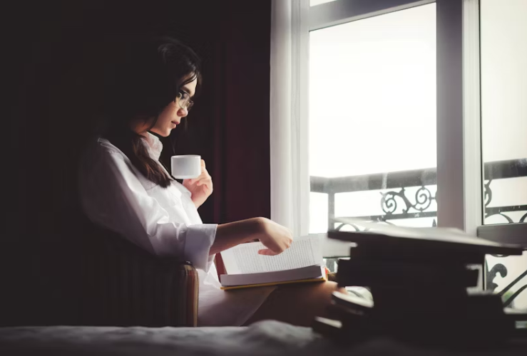 창가에 앉아 커피를 마시며 책을 읽고 있는 여성의 고요한 모습