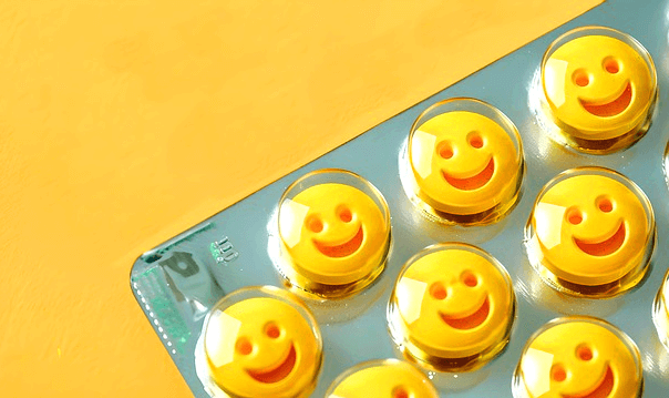 회색 포장지 안에 노란 알약들이 가득하다. 알약이 해맑게 웃는 표정을 짓고 있다.