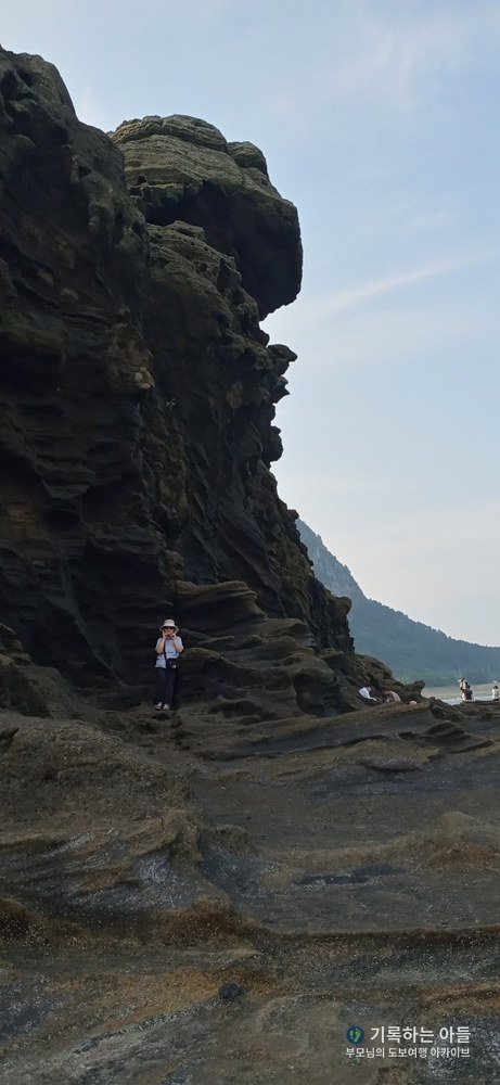 용머리해안 거대한 화산암 벽 아래 작게 선 어머니