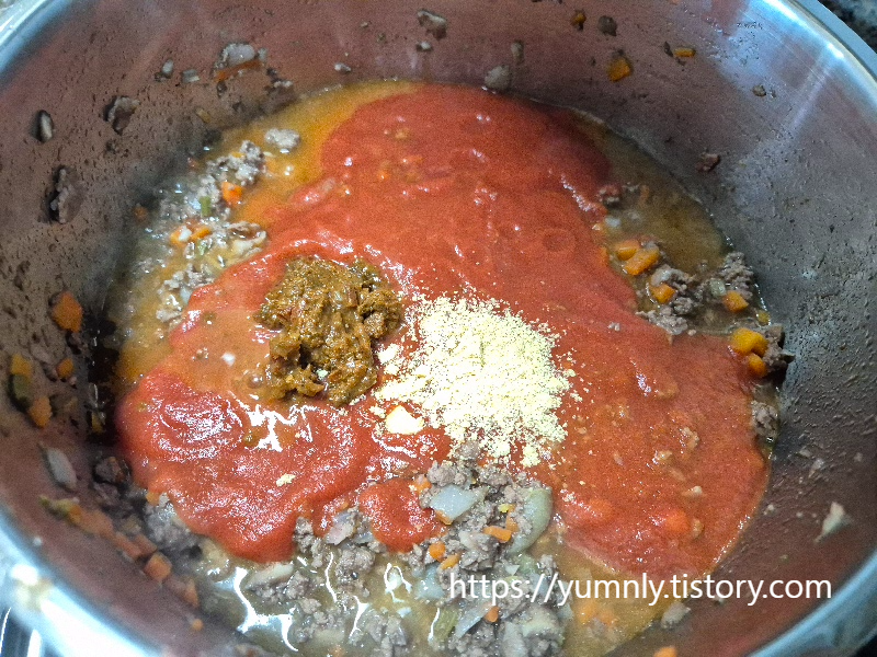 Adding tomato puree, chicken stock, and tomato paste to the pot for the ragu sauce