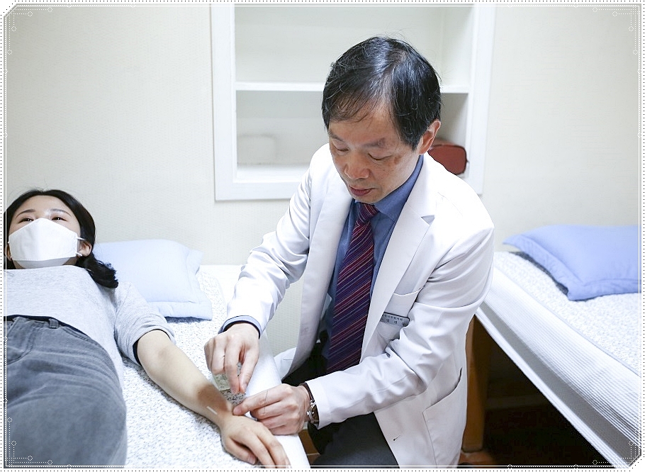 누워 있는 환자의 손 등에 침을 놓고 있는 한의사의 모습
