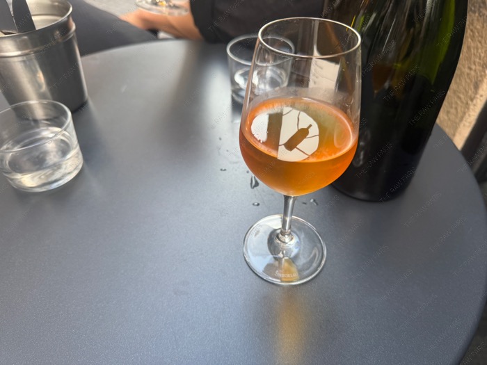 A glass of orange natural wine served on an outdoor bistro table at Le Dénicheur Paris