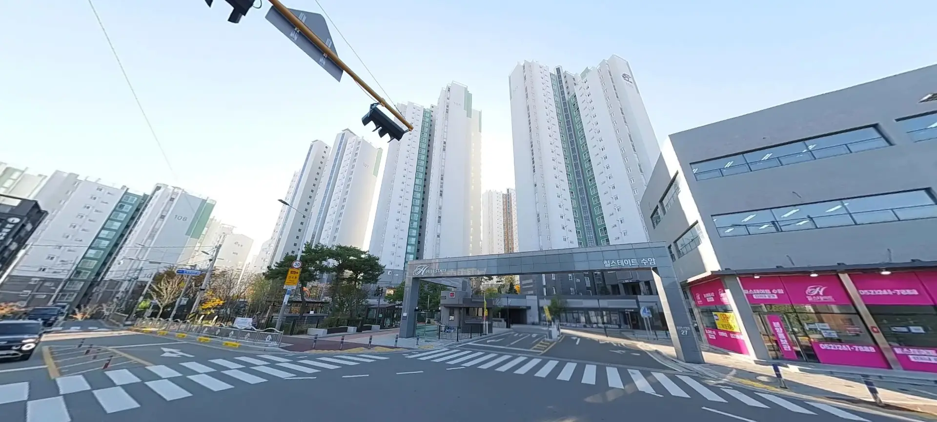 울산 공무원아파트 힐스테이스수암 입구의 모습이다. 아파트 전경이 보이고 오른쪽에 부동산이 보인다.