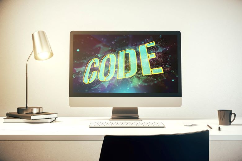 깔끔한 화이트 책상 위 데스크탑 모니터 화면에 우주 배경의 CODE 3D 텍스트가 표시되어 있고, 램프, 노트, 키보드, 커피잔이 놓인 미니멀한 프로그래밍 작업 환경 이미지