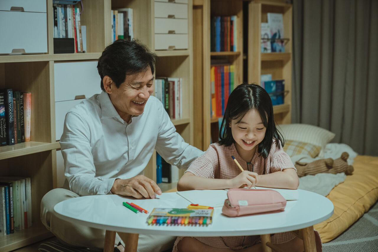 테이블에 앉아 웃으며 숙제하는 손녀와 손녀를 바라보며 웃는 할아버지