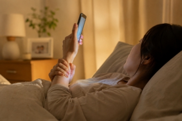 육아 후 침대에서 스마트폰을 보는 부모의 손목과 목 피로를 표현한 감성 라이프스타일 이미지