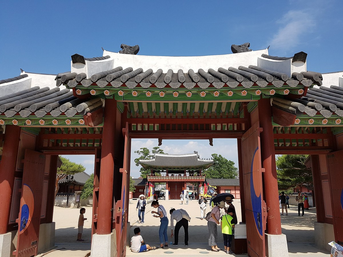 Red gate pavilion and sand courtyard of Hwaseong Haenggung palace in Suwon with visitors under a blue sky