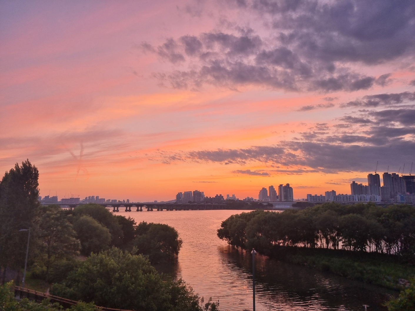 한강을 배경으로 한 평화로운 풍경. 잔잔한 물결 위에 다리가 놓여 있고, 주변에는 녹지가 펼쳐진 단순한 일러스트 풍경