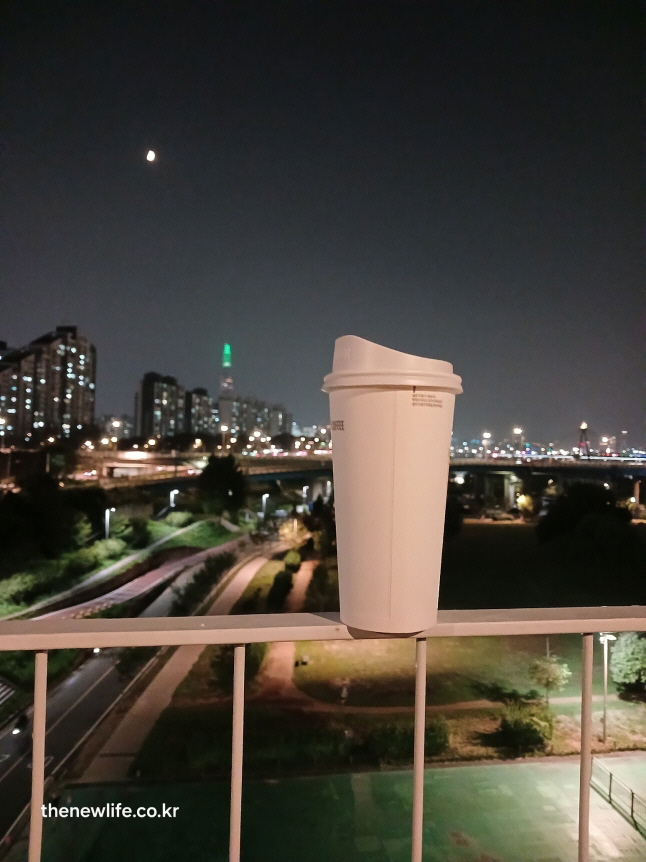 운동후 롯데타워 불빛을 배경으로 난간 위에 놓인 테이크아웃 커피 컵