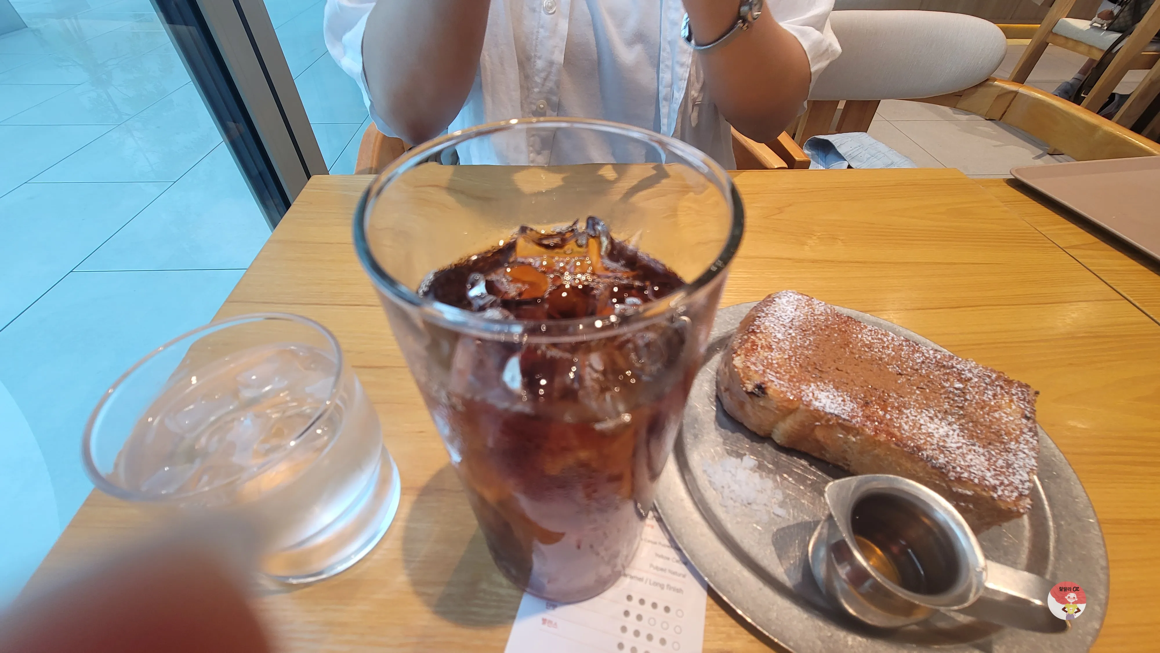 카페 테이블 위 아이스 아메리카노&amp;#44; 물컵&amp;#44; 프렌치토스트와 시럽잔이 놓인 모습
