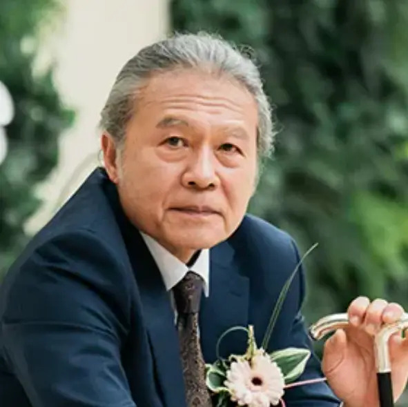 야외에서 지팡이를 짚고 파란양복을 입은 흰머리의 강상모