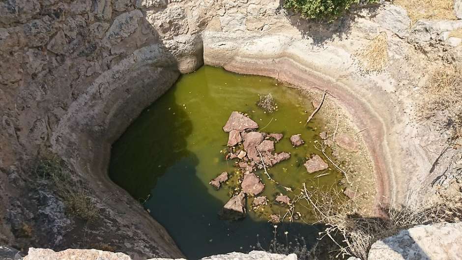 미케네 유적지에 남아 있는 원형 석조 우물 내부에 고여 있는 녹색 물과 돌들이 보인다.