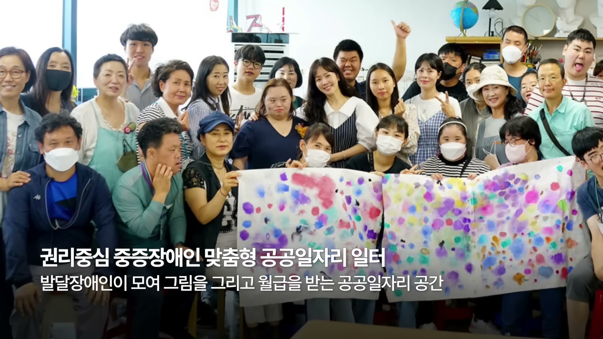화실에서 발달장애인과 활동가 30여 명이 단체로 모여 색색의 점이 가득한 그림 두 폭을 들고 함께 카메라를 향해 웃고 있는 단체 사진