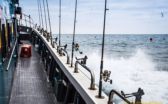 낚시배가 바다를 가르며 나가는 모습. 낚시대가 꽂혀있다.