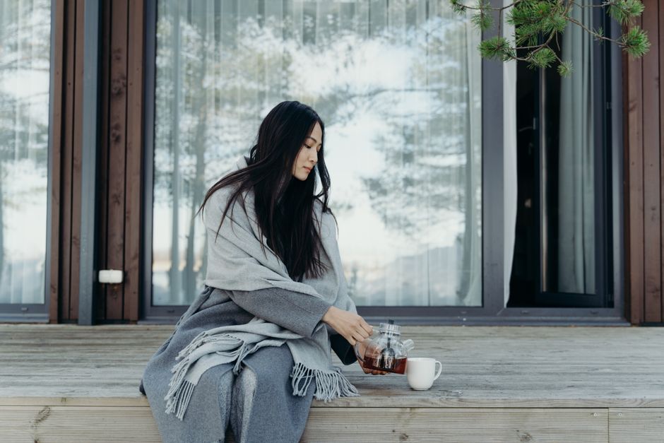Serene moment of a woman pouring tea outdoors, wrapped in a cozy blanket.