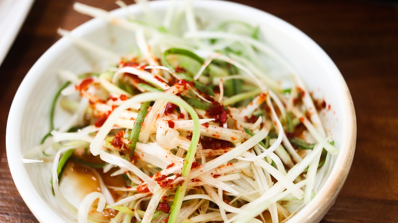 Green onion salad (파절임) seasoned with red pepper flakes and soy sauce, served in a white bowl on a wooden table.