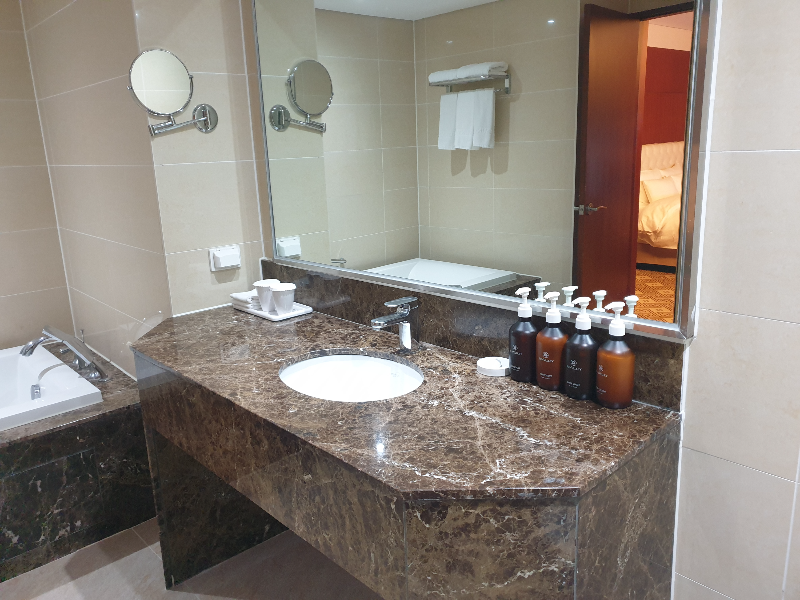 세면대 위에 삼푸, 린스, 로션, 컨디셔너 세트가 보인다. 왼쪽에 욕조도 살짝 보인다.