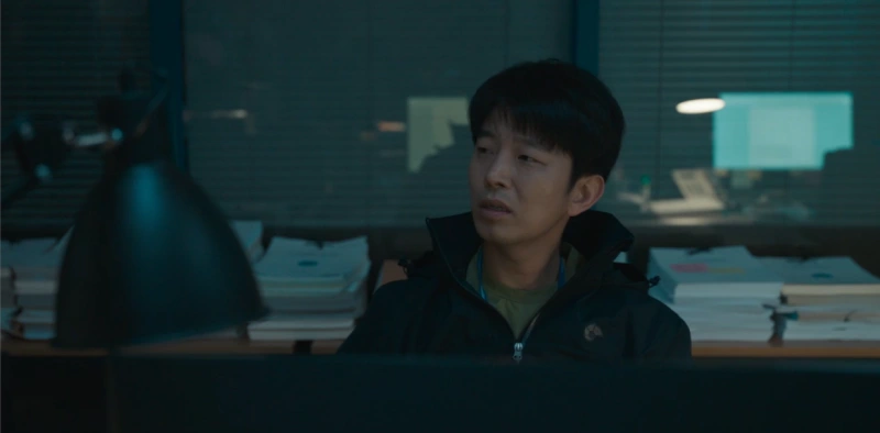 경찰서 책상을 배경으로 검은 점퍼를 입고 앉아 있는 드라마 유괴의 날 창훈 캐릭터