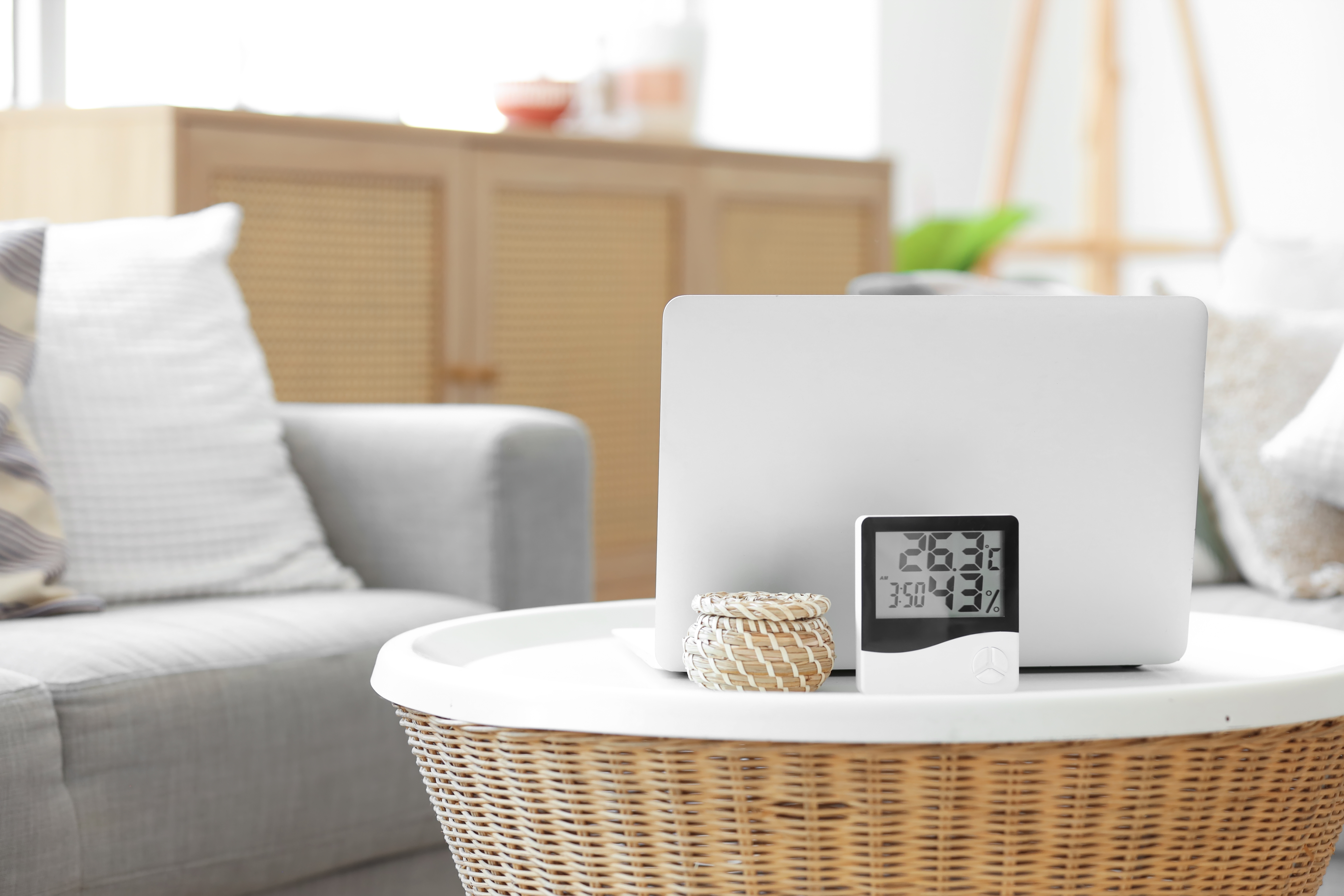 실내 테이블 위에 놓인 디지털 온습도계와 노트북, 여름철 실내 습도 관리를 보여주는 거실 환경