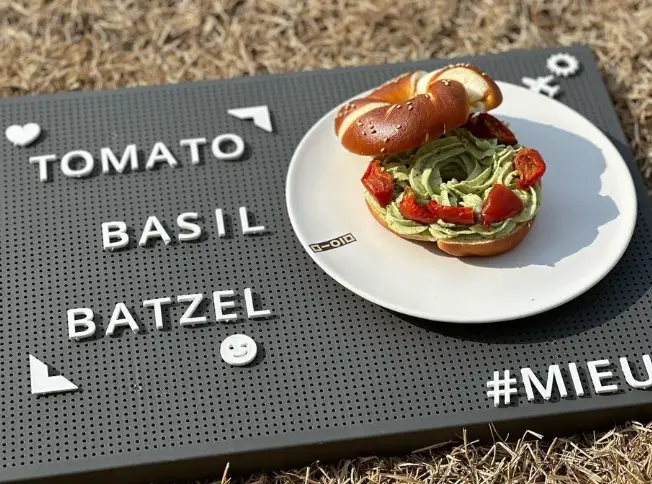 겨울방학 국내 여행지- 잔디위 회색 쟁반 위 흰접시 위 가로로 반이 잘린 베이글 빵단면 초록색 크림위 딸기가 얹혀진 이미지