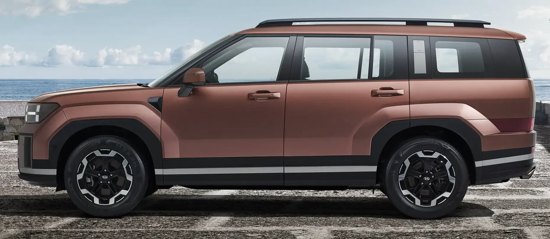 회색 시멘트 바닥 뒤 파란바다와 푸른하늘을 배경으로 서있는 갈색 싼타페 자동차