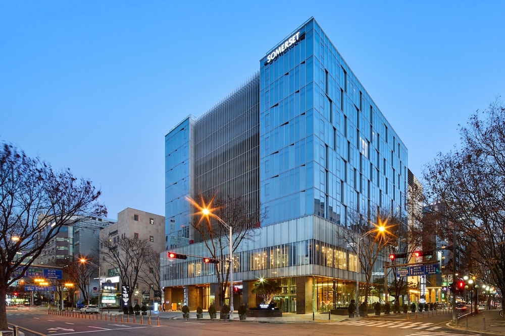 경기도 성남시 분당구에 위치한 서머셋 센트럴 분당 호텔 외관. 유리로 둘러싸인 모던한 고층 건물이 도심 한가운데 세련된 분위기를 자아내며, 해 질 무렵 따뜻한 가로등 불빛이 어우러진다.