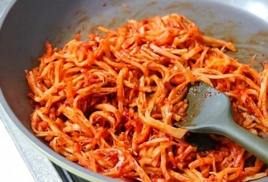 회색 볶음팬에서 실리콘 조리도구를 사용해 매콤한 양념에 버무려지고 있는 진미채볶음.