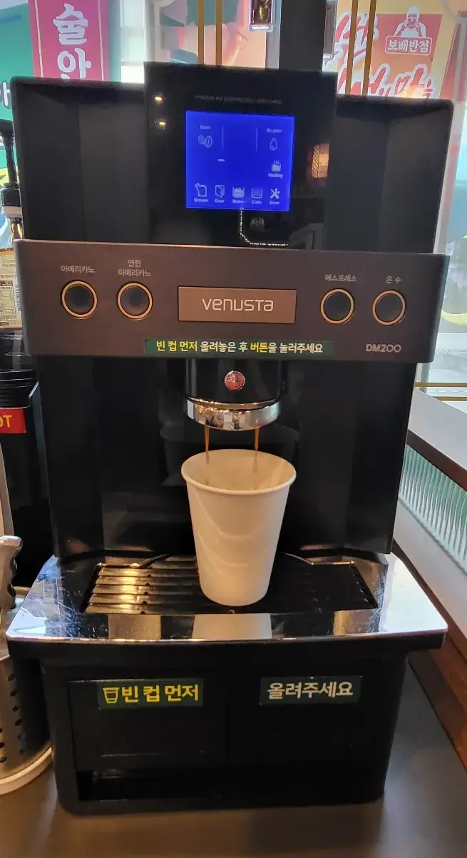 보배반점 - 아메리카노 커피 기계에서 나오는 커피액체가 종이컵에 담기는 이미지