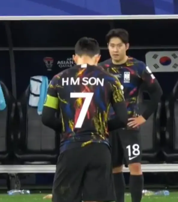 손흥민- 검은색, 붉은색, 파란색이 섞인 국가대표 유니폼을 입고 고개숙인 손흥민 뒷모습과 국가대표 유니폼을 입고 손흥민을 바라보는 이강인