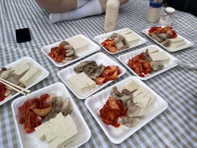 흰색 일회용 접시에 담긴 두부와 고기와 김치